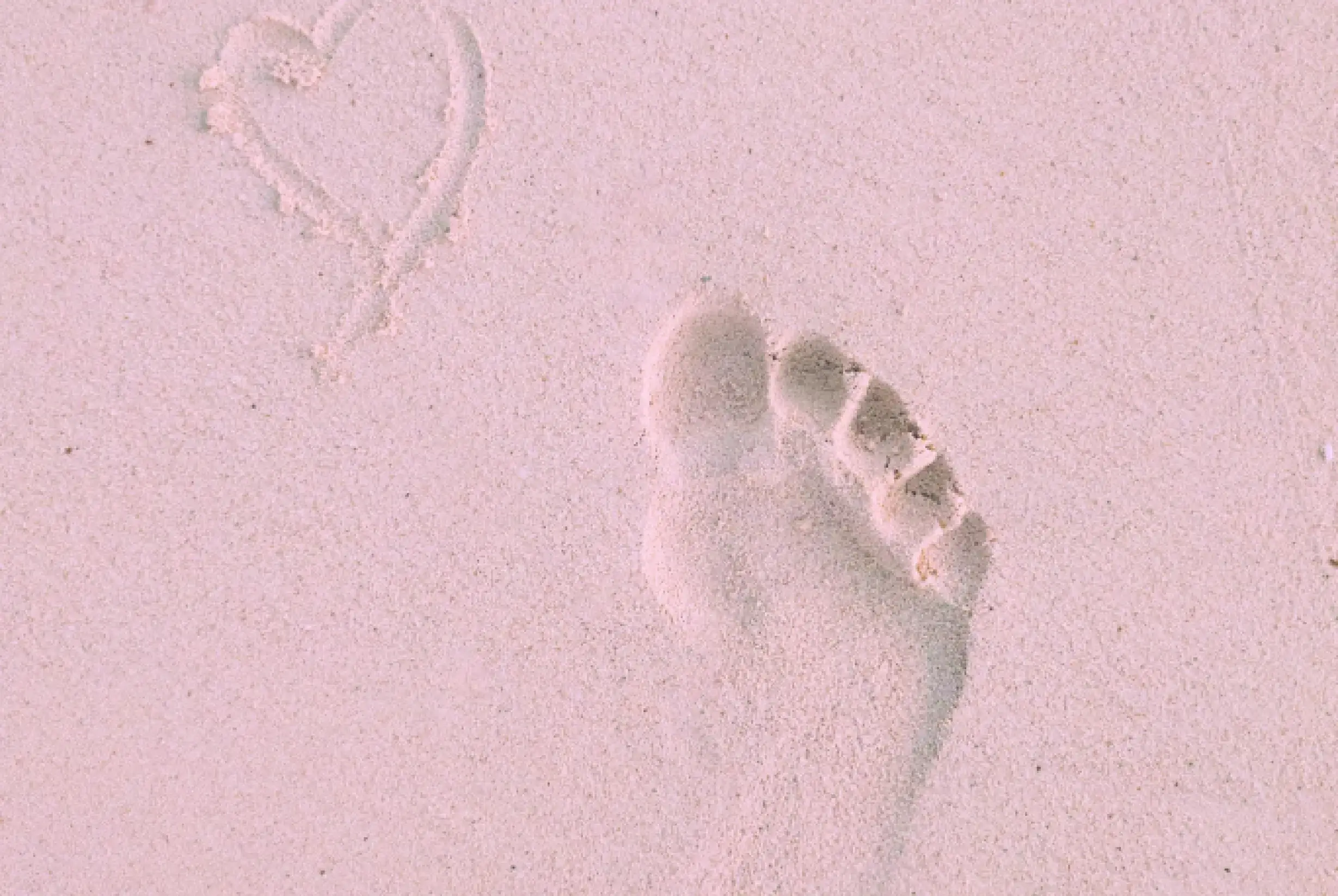 Footprint on a pink sand beach next to a heart